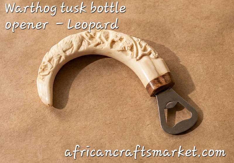 Warthog tusks bottle openers -leopards A genuine African warthog tusk bottle opener featuring a detailed, hand-carved 3D relief sculpture of a leopard along the natural curve of the ivory handle.